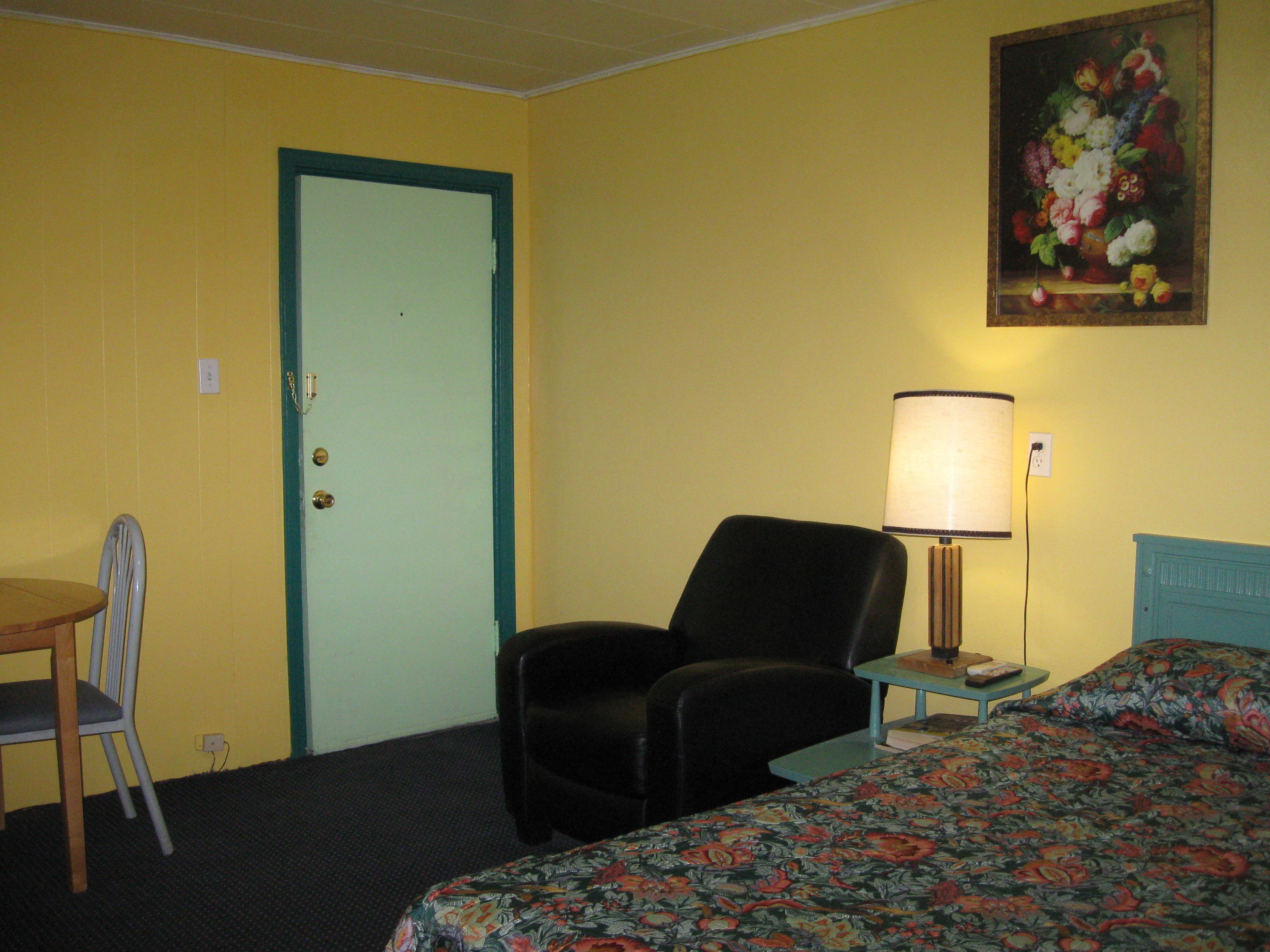 Una habitación de hotel con cama, una silla, un escritorio, una lámpara y una puerta.