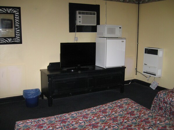 A hotel room with a television on a black dresser, a microwave on top of a refrigerator, and a patterned bedspread.