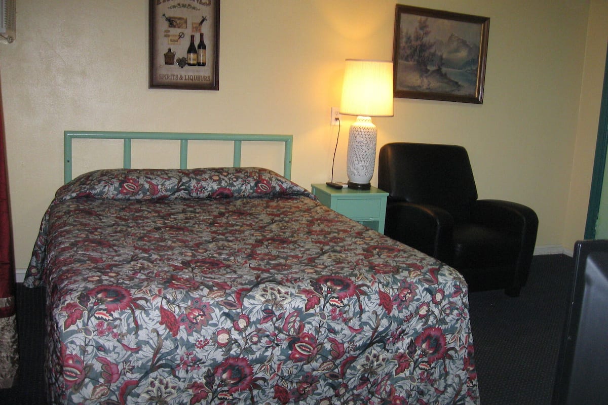 A hotel room with a floral bedspread, a framed poster on the wall, a lamp, and a chair.