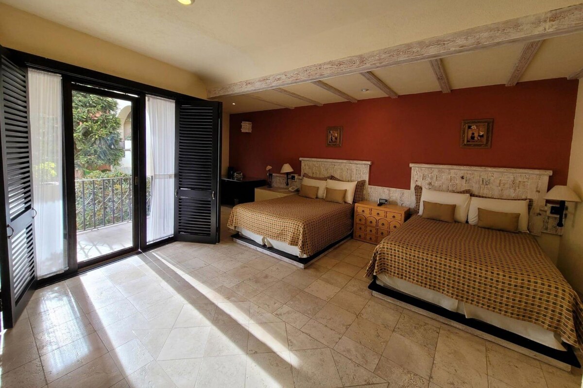 Habitación de hotel con dos camas, un balcón y vistas a zonas verdes.