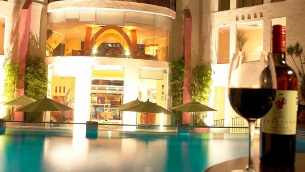 A poolside area with a lounge chair, a bottle of wine, and a glass of wine on a table.