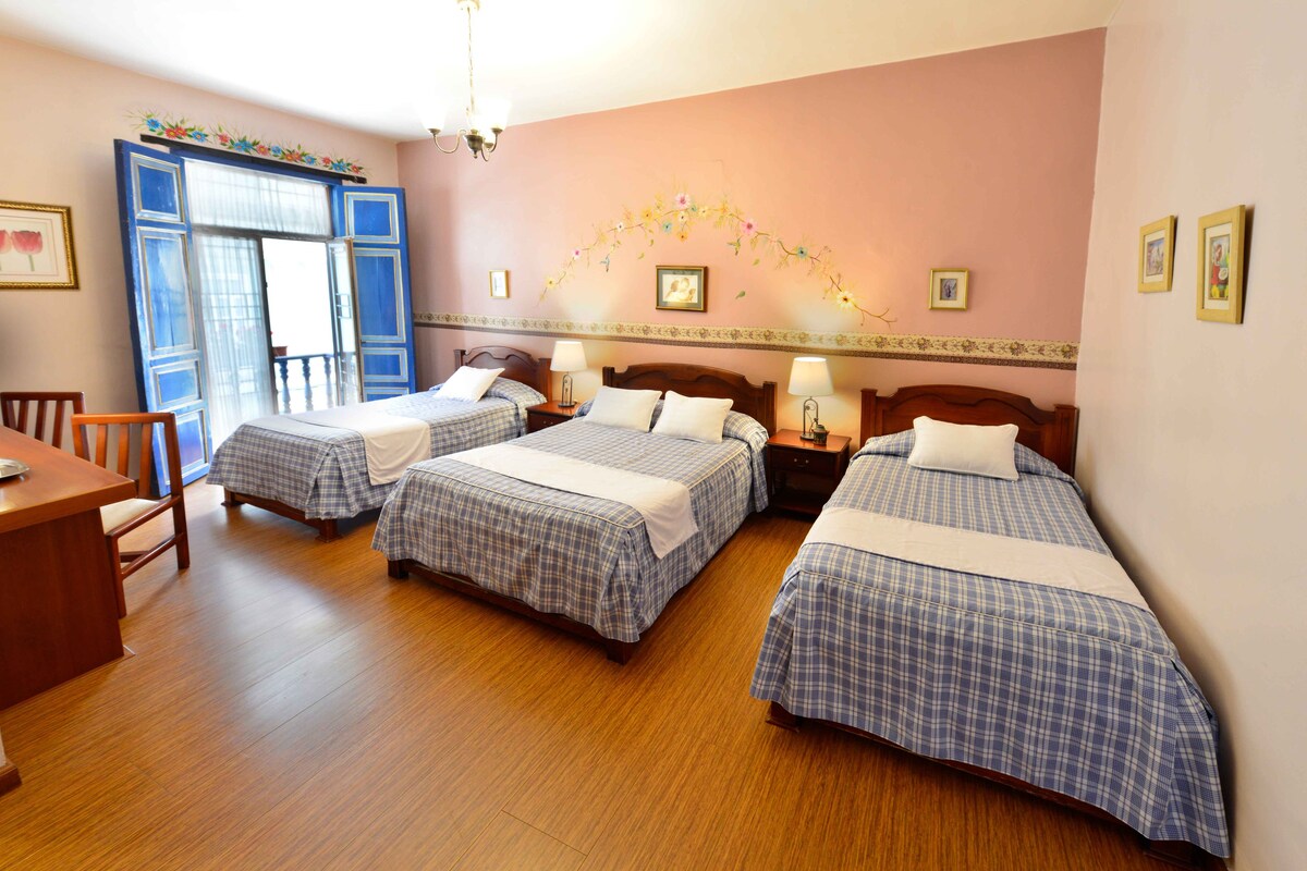 A hotel room with three beds, a wooden desk, and a chair.