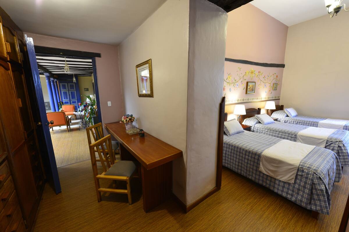 Habitación de hotel con dos camas, un escritorio y una silla. Hay un espejo en la pared y una ventana con cortinas.