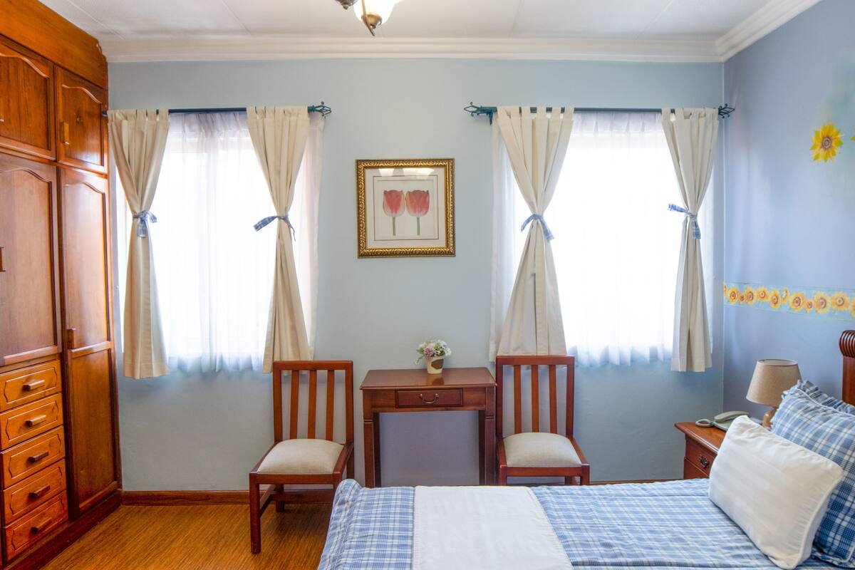 Un dormitorio con cama, dos sillas, una mesita de noche, un escritorio y un aparador.