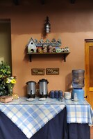 Uma mesa com toalha xadrez azul e branca, dois preparadores de café, um dispensador de água e um letreiro indicando 'Aqua Water' e 'Cafe Coffee'.