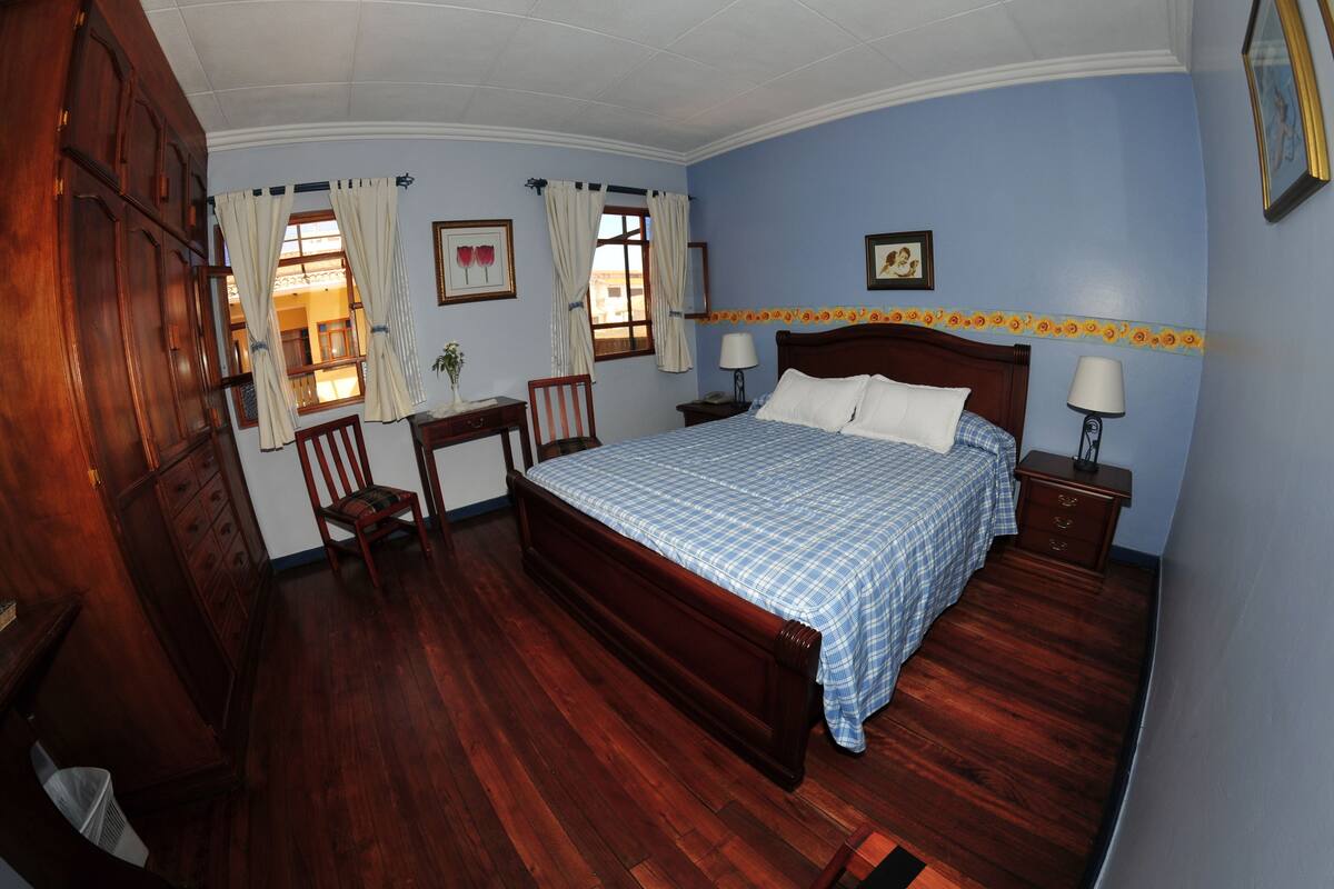 Un dormitorio con una cama de madera, dos mesitas de noche, una silla y un escritorio.