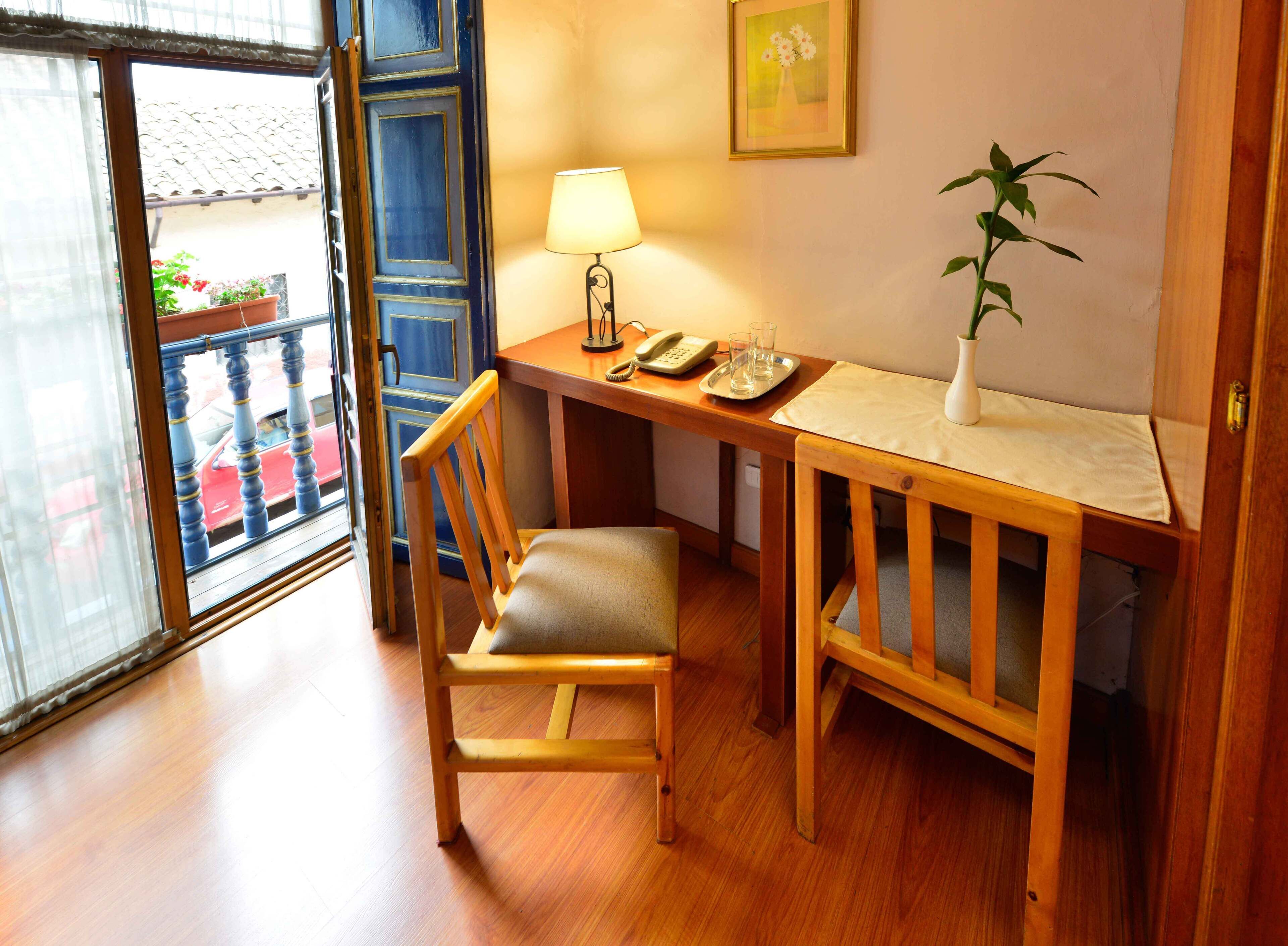 A wooden desk with a chair, a lamp, a vase with a plant, and a framed picture on the wall.
