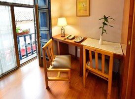 A wooden desk with a chair, a lamp, a vase with a plant, and a framed picture on the wall.