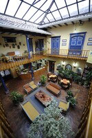 A spacious indoor area with a high ceiling, a central seating area with tables and chairs, and a balcony with a railing.