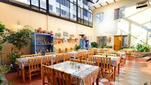 Um restaurante com várias mesas e cadeiras, piso de azulejos e plantas e decorações nas paredes.