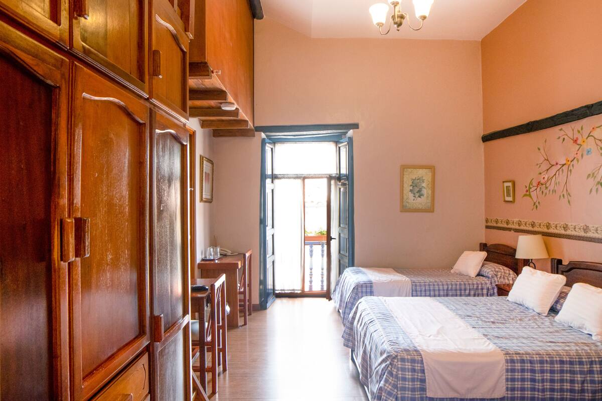 Habitación de hotel con dos camas, muebles de madera y vistas a través de una puerta abierta.