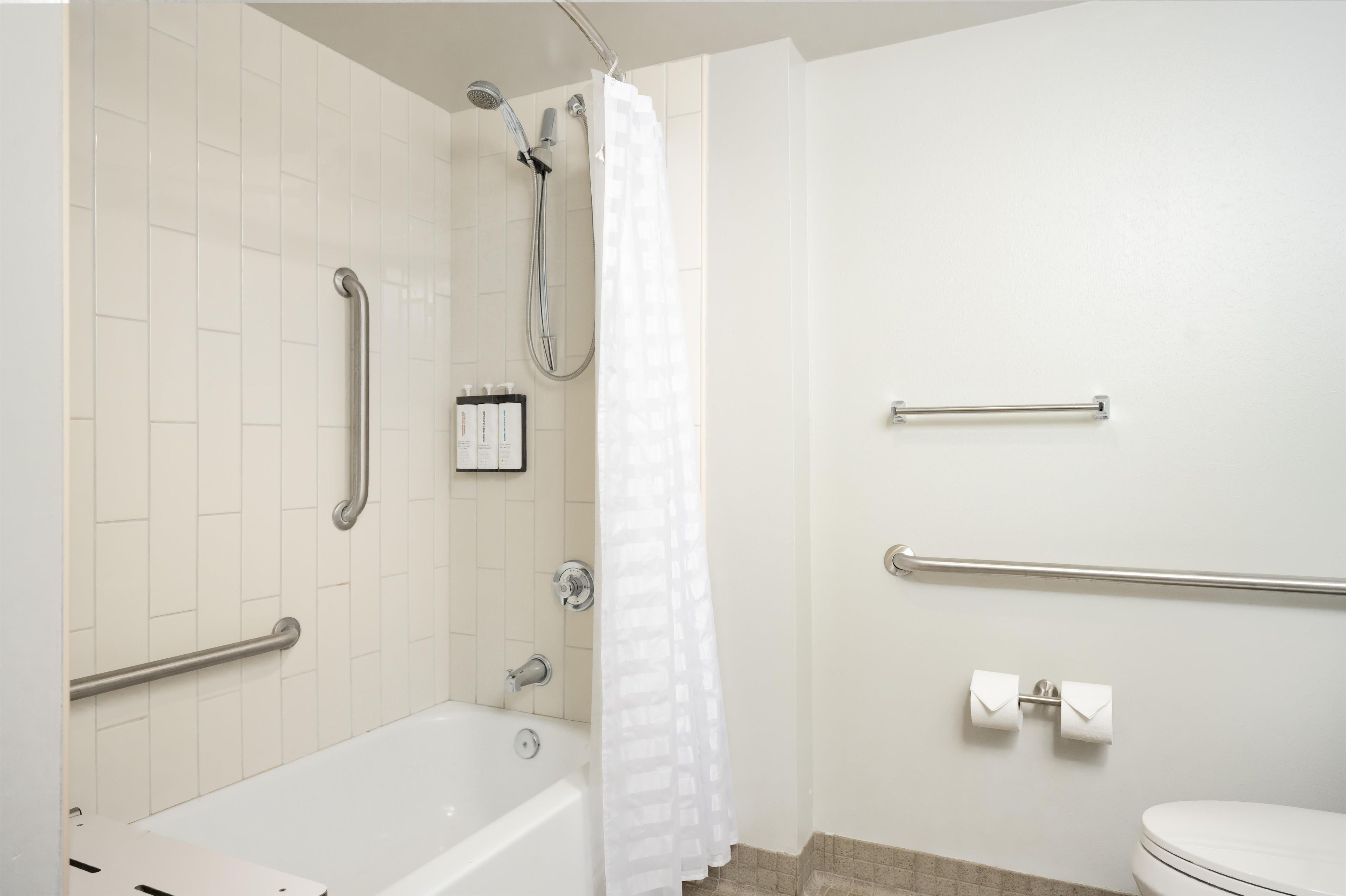 Un baño con bañera, ducha e inodoro. Se han instalado barras de apoyo cerca de la bañera y el inodoro.