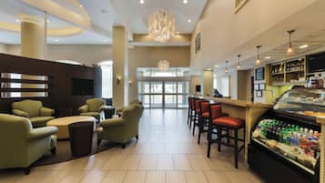 A modern hotel lobby with seating areas, a bar, and a food display.