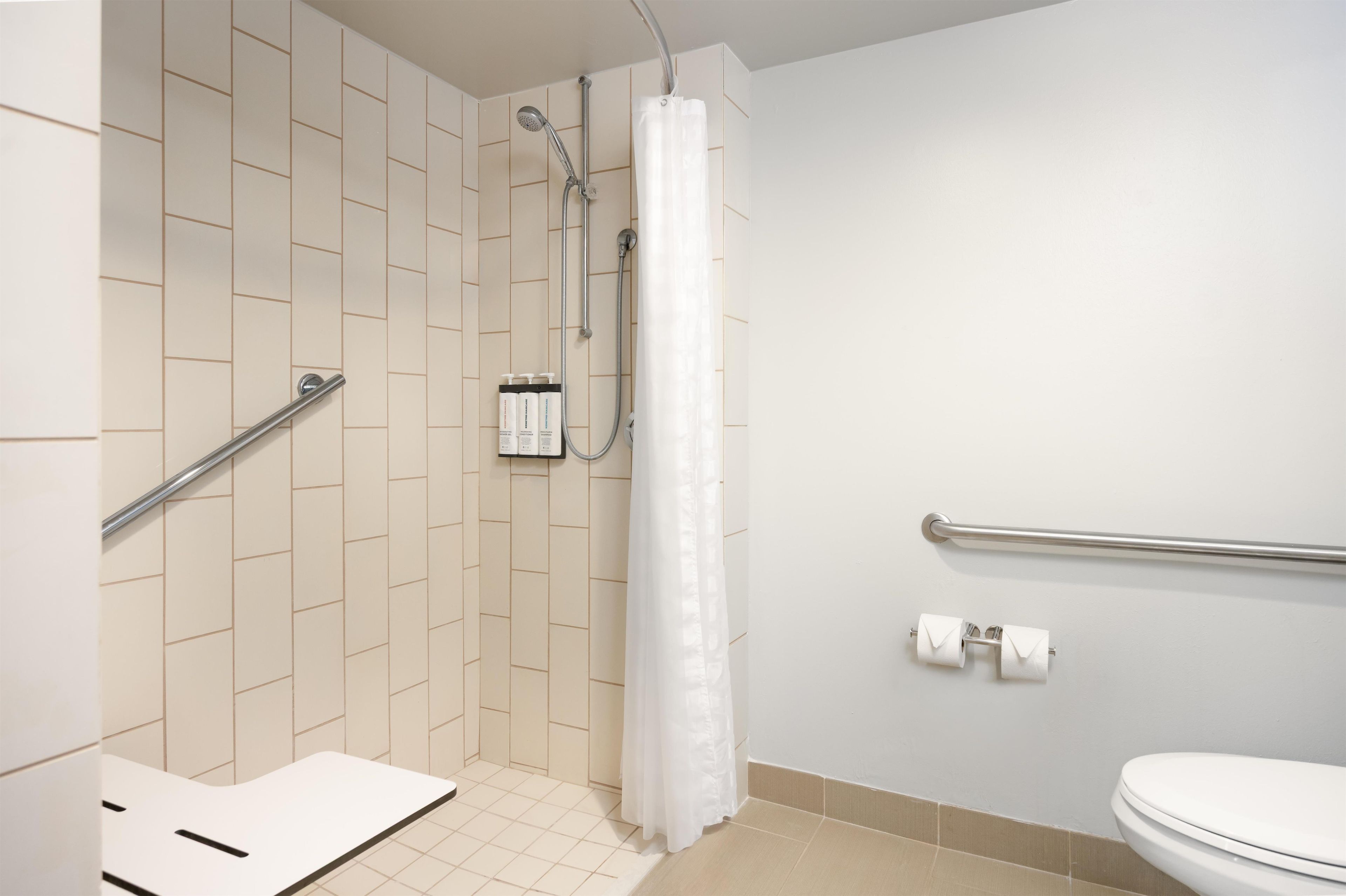 A bathroom with a shower, toilet, and handrails.