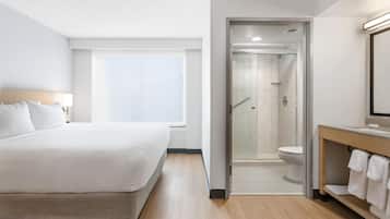 Una habitación de hotel con una cama, zona de ducha y baño con inodoro y lavabo.