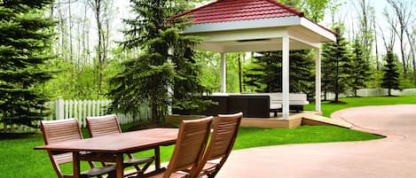 A gazebo with a red roof, a wooden table with chairs, and a white picket fence in the background.