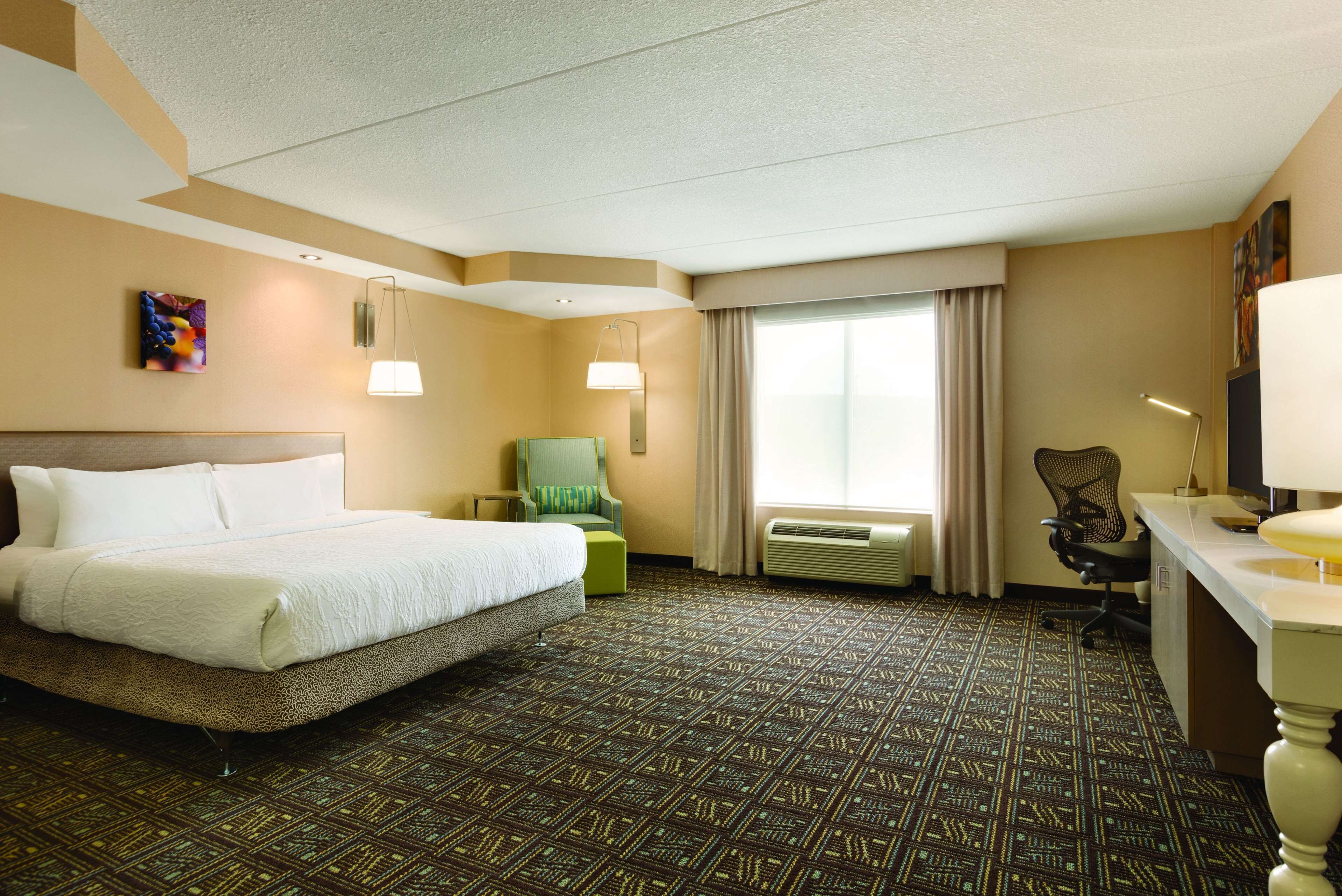 A hotel room with a large bed, a desk, a chair, and a window with curtains.