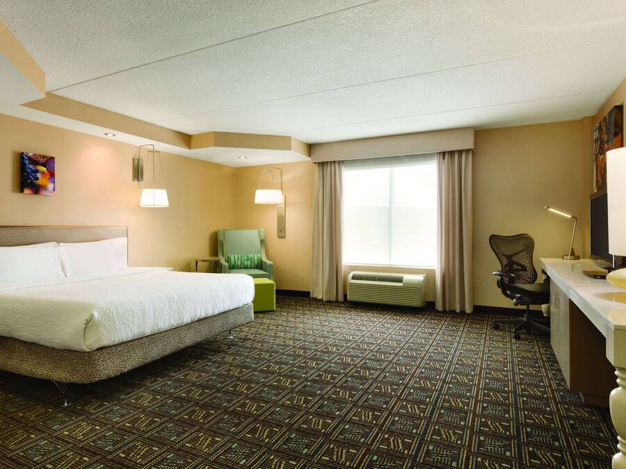 A hotel room with a large bed, a desk, a chair, and a window with curtains.