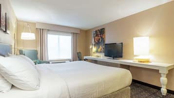 A hotel room with a large bed, a desk with a flat-screen TV, a lamp, and a window with curtains.