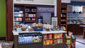 A coffee shop with a refrigerated display, shelves stocked with snacks, and a sign advertising specialty coffee. - Hilton Garden Inn Niagara-on-the-Lake (Niagara-on-the-Lake)