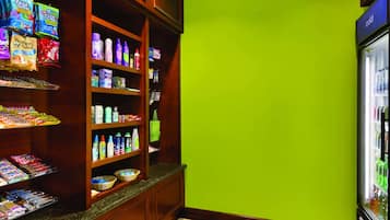 Une chambre d’hôtel avec un mur vert, une étagère en bois contenant des en-cas et des articles de toilette, et un réfrigérateur sur lequel est apposé un panneau indiquant « froid ».