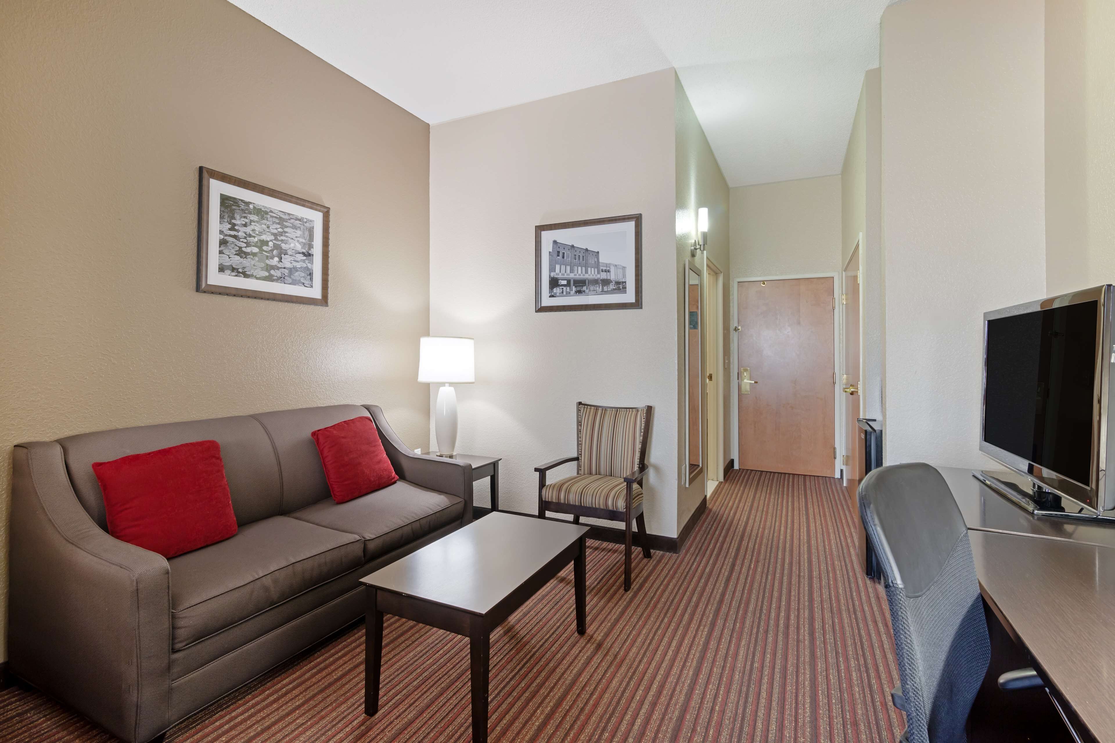 A hotel room with a sofa, armchair, TV, and framed pictures on the walls.