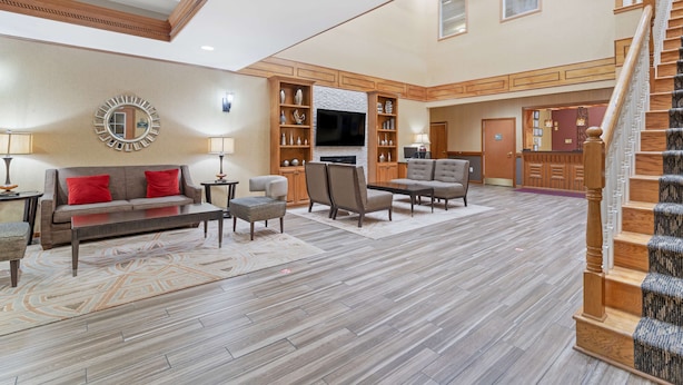 A spacious living area with a sofa, chairs, a coffee table, and a fireplace. There is a television mounted above the fireplace and a staircase leading to another level. - Best Western Plus Bradbury Inn & Suites (Waycross)