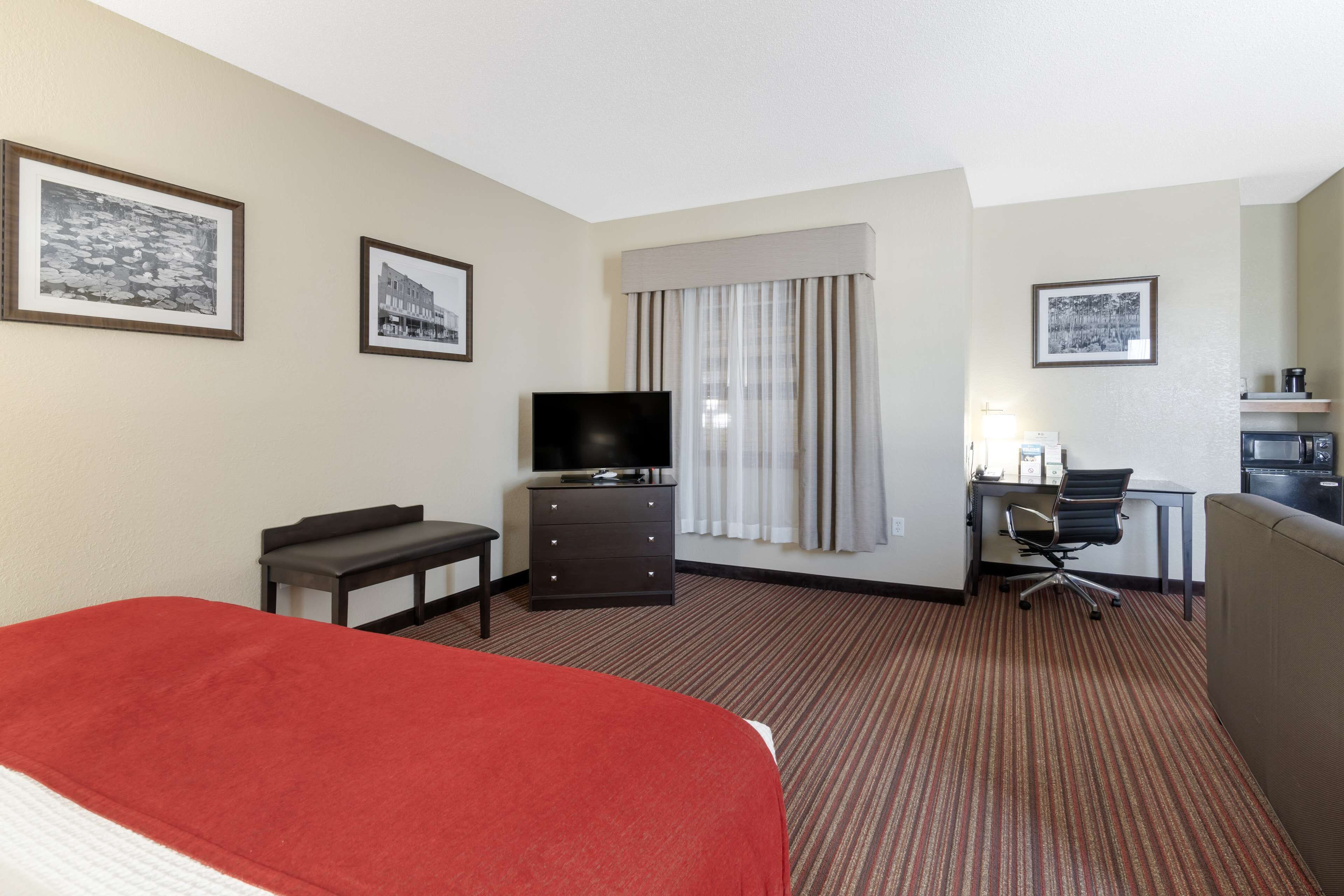 A hotel room with a bed, a desk with a computer, a TV, and a window with curtains.