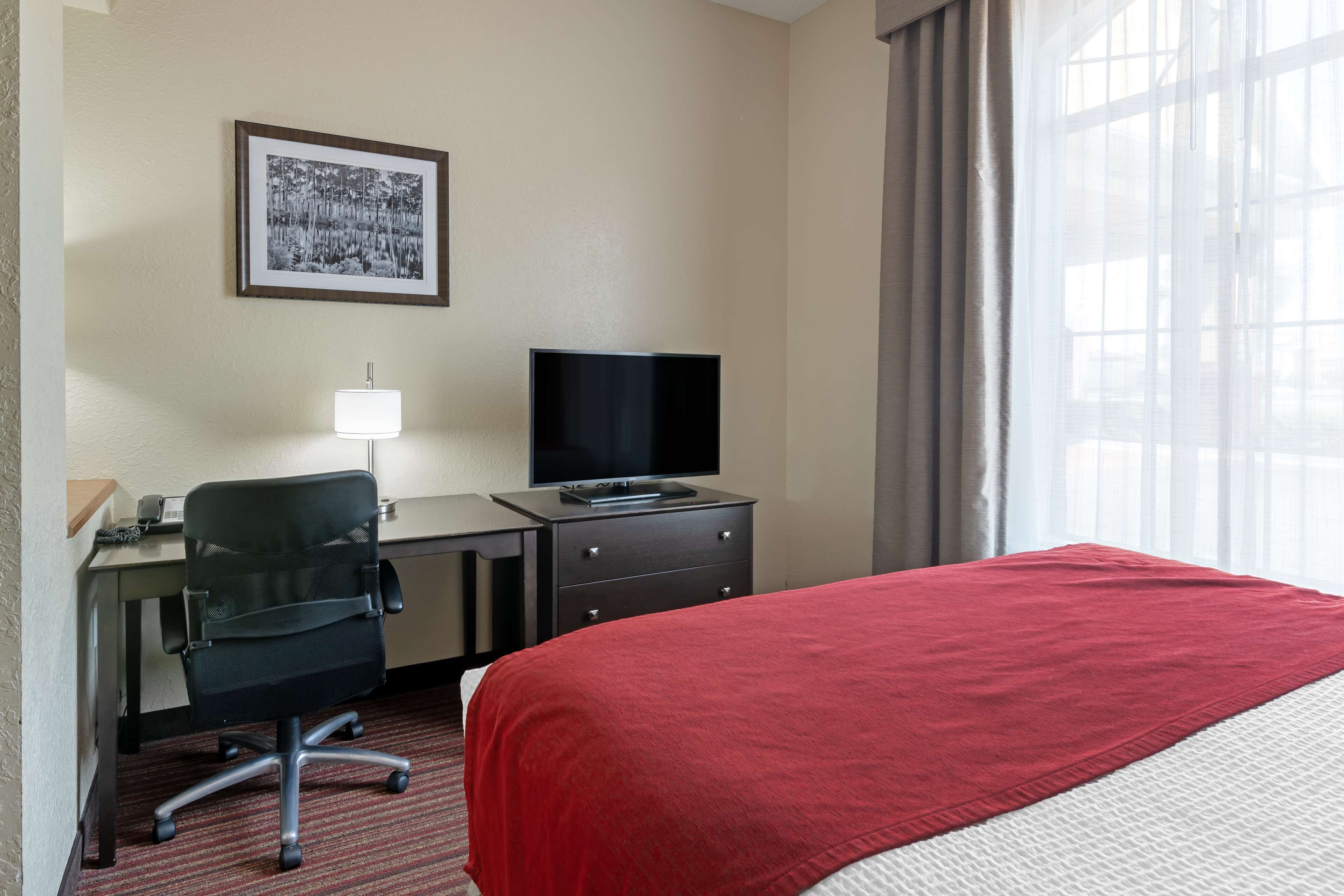 A hotel room with a bed, desk, chair, television, and a framed picture on the wall.