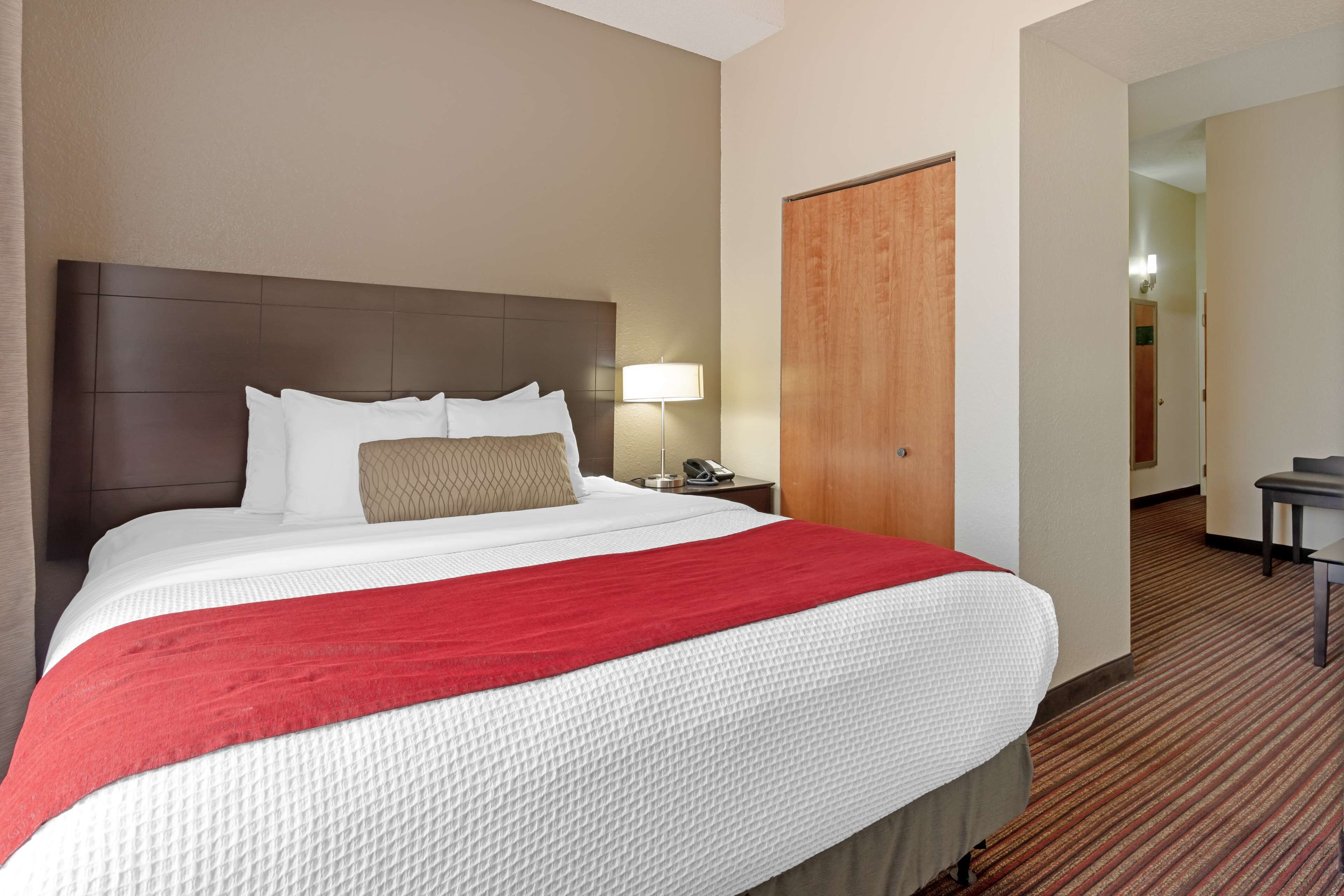 Een hotelkamer met een groot bed, een nachtkastje met een lamp en een houten deur.