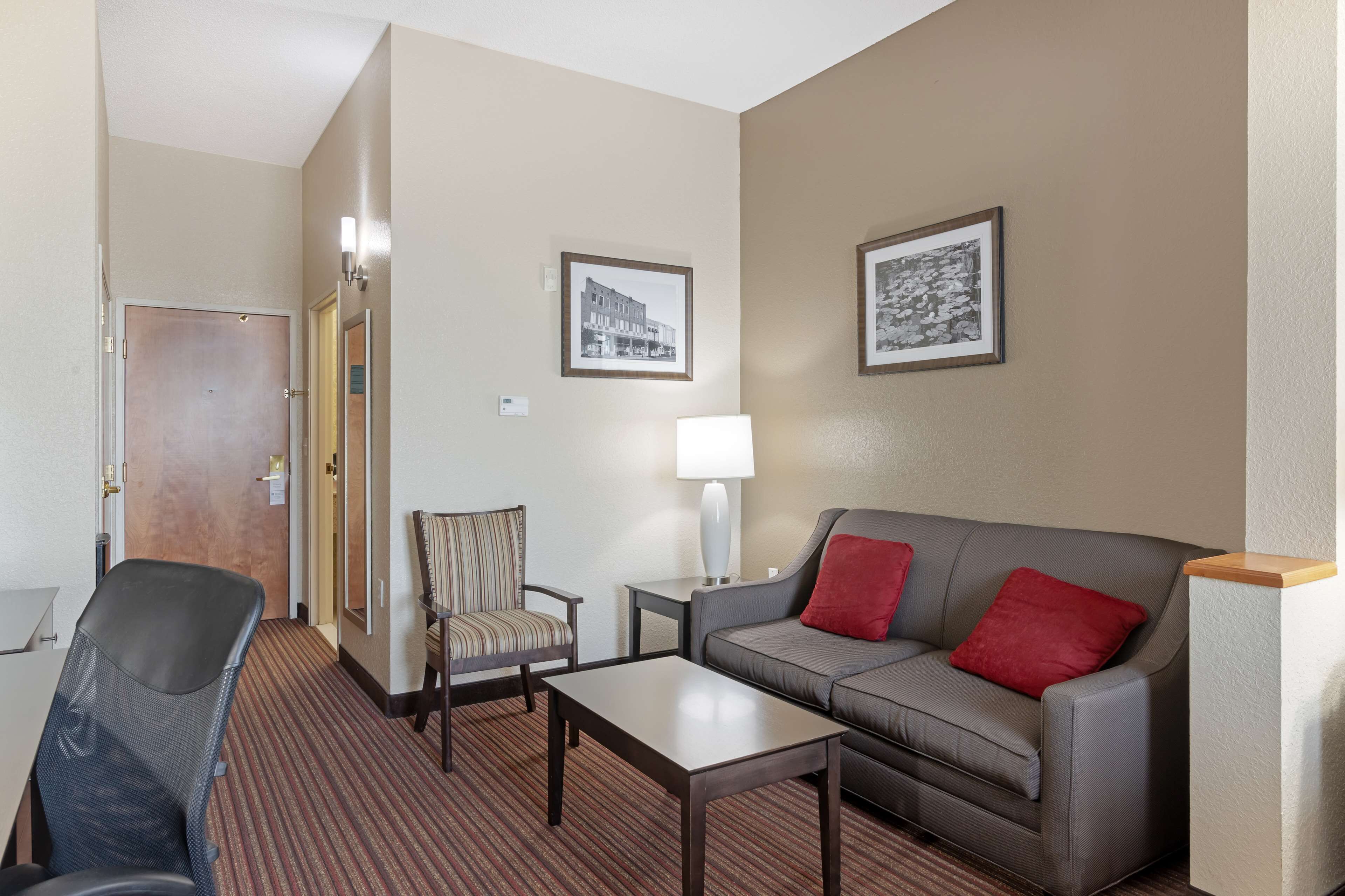 A hotel room with a sofa, armchair, coffee table, and a door leading to another room.