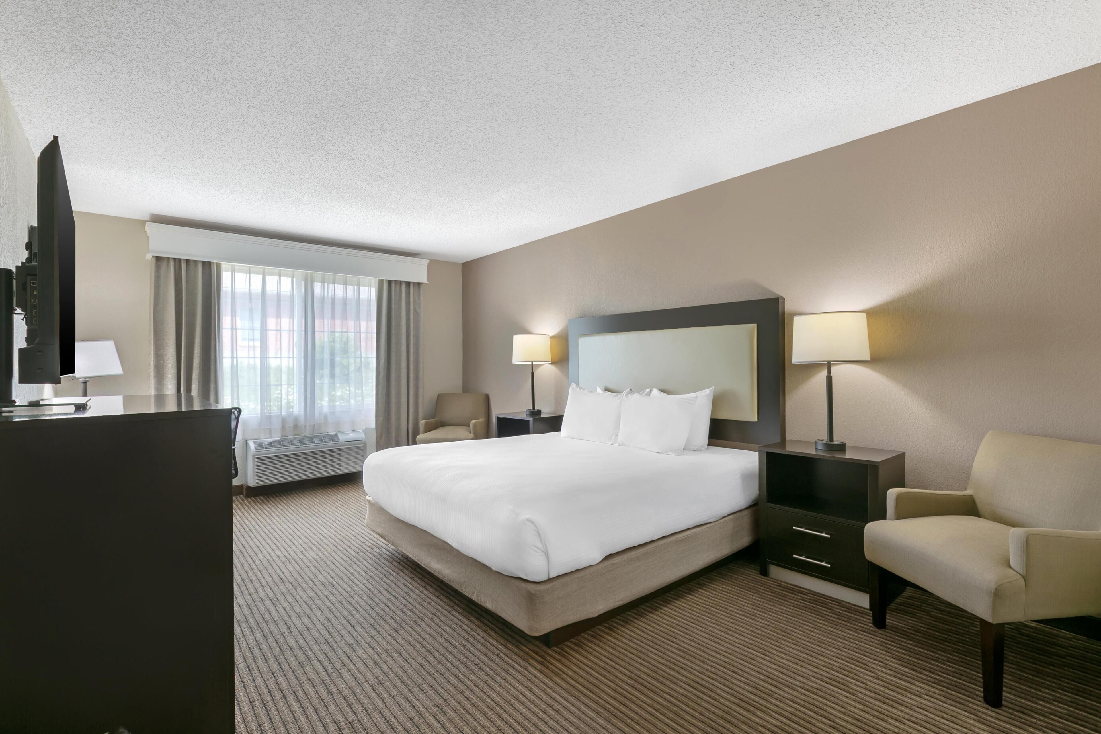A hotel room with a large bed, two bedside tables with lamps, a chair, a desk, and a TV.