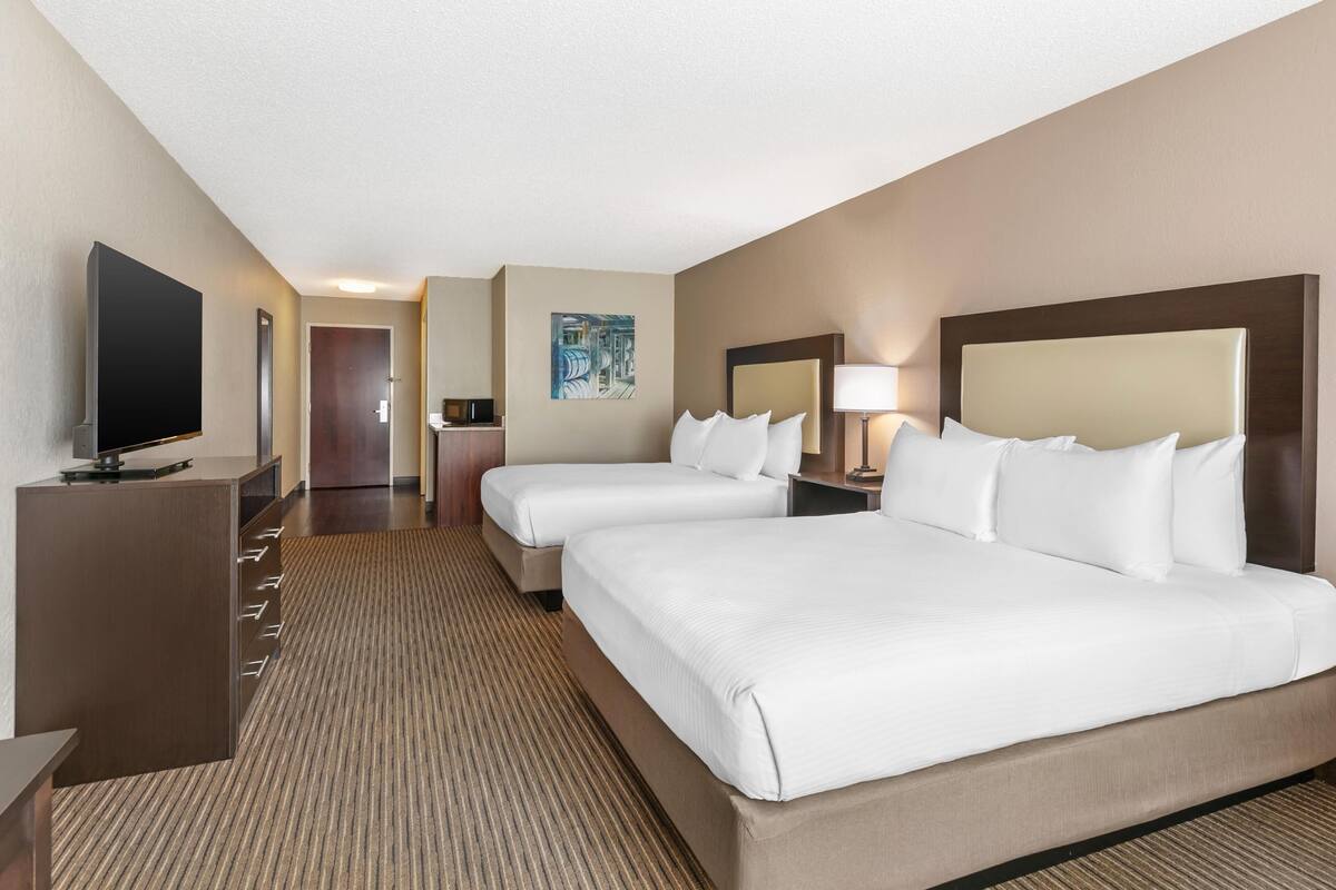 A hotel room with two beds, a TV, a desk, and a painting on the wall.