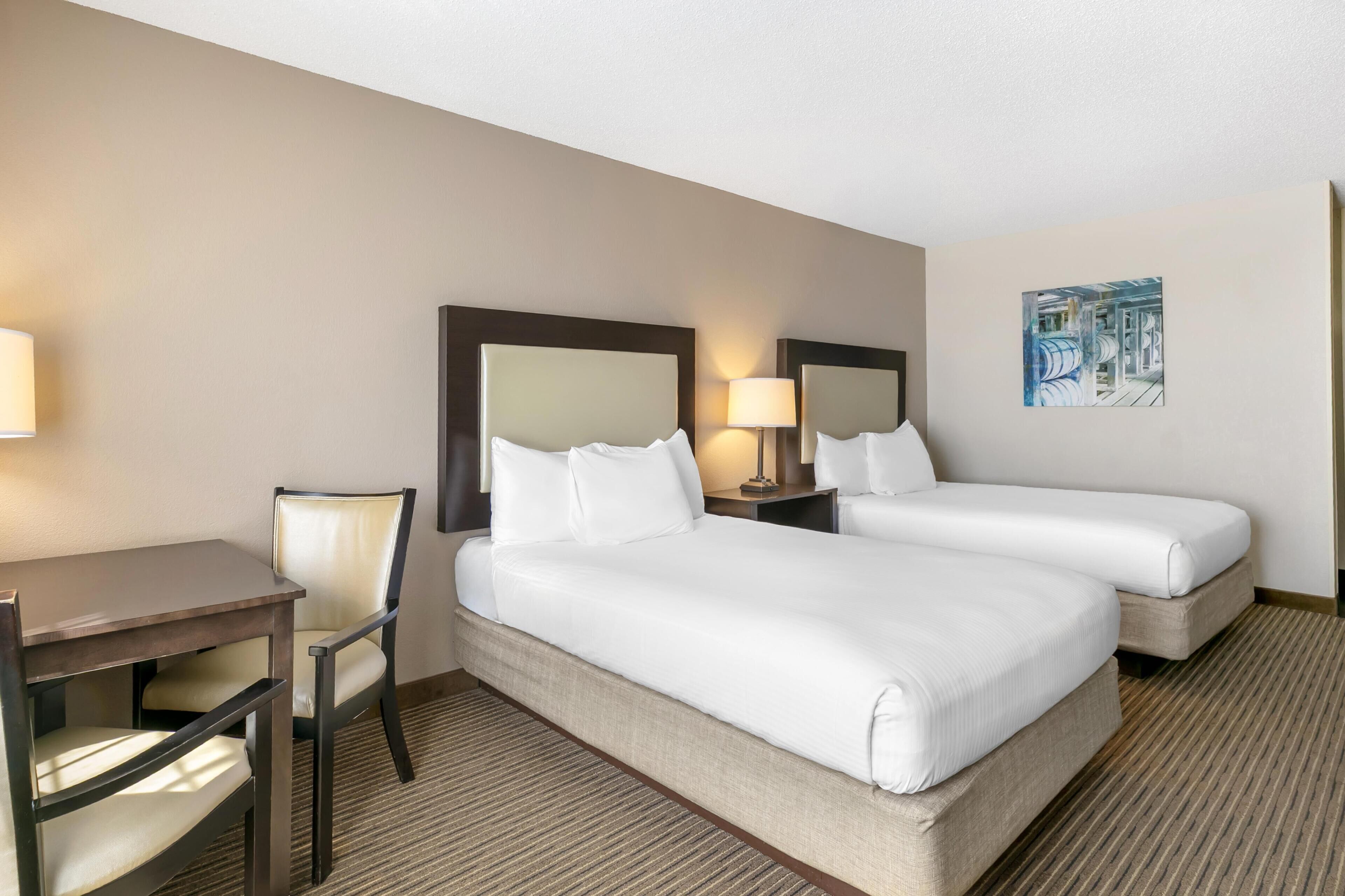 A hotel room with two beds, a desk, a chair, and a painting on the wall.