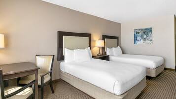 A hotel room with two beds, a desk, a chair, and a painting on the wall.