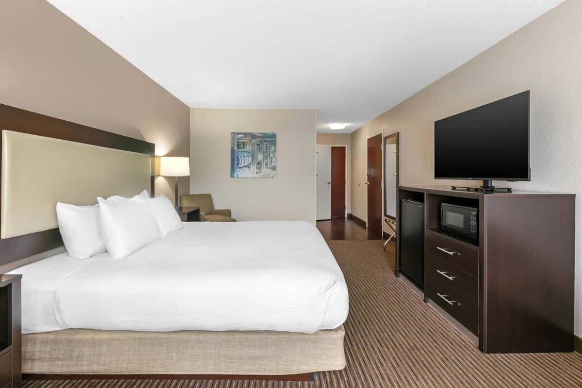 A hotel room with a large bed, a flat-screen TV, a desk with a lamp, and a microwave.