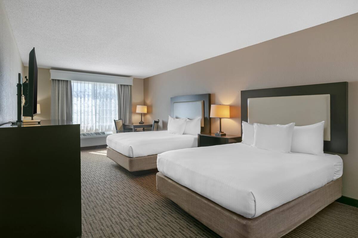 A hotel room with two beds, a desk, a chair, and a television.