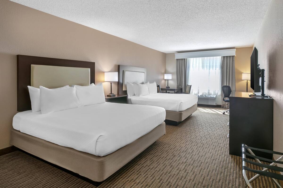 A hotel room with two beds, a desk, a chair, a TV, and a city view.