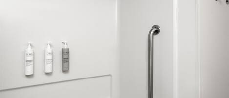 A modern bathroom with a shower, a handrail, and three bottles of shampoo.