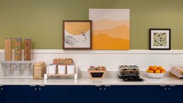 A kitchen with a white countertop, blue cabinets, and various food items and kitchen appliances.