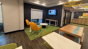 Un espacio de oficina moderno con una pantalla grande, sillas amarillas y una mesa de madera.