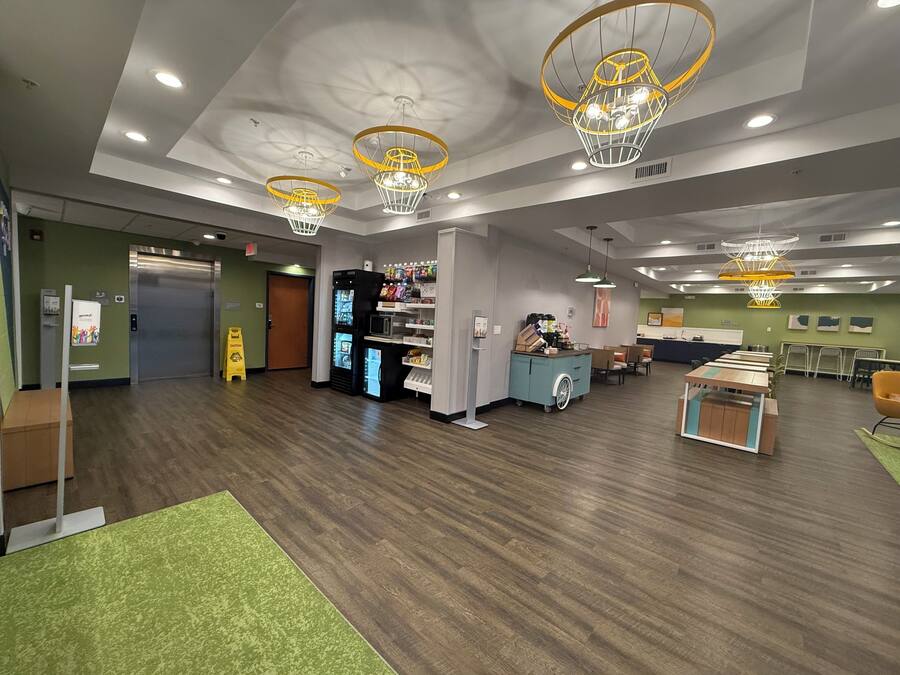 Un hall d’entrée spacieux doté d’un plancher en bois, d’un distributeur automatique, d’un comptoir de réception et d’un espace détente avec des chaises et des tables.