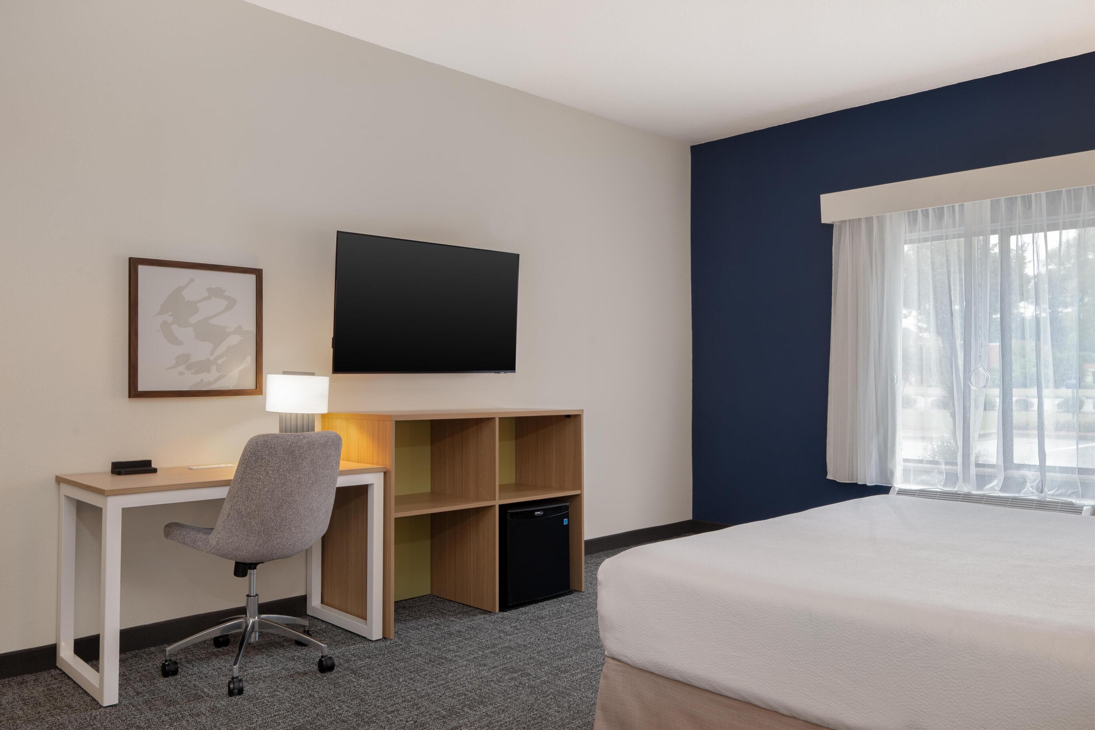 Una habitación de hotel con cama, escritorio, silla, televisor y un pequeño armario.