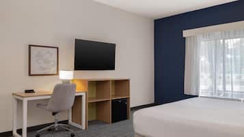 A hotel room with a bed, desk, chair, TV, and a small storage unit.