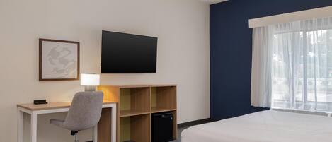 Una habitación de hotel con cama, escritorio, silla, televisor y un pequeño armario.