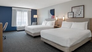 Habitación de hotel con dos camas, un escritorio, una silla, una ventana con cortinas translúcidas y decoración en la pared.