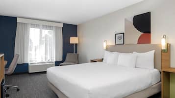 Una habitación de hotel con una cama grande, un escritorio, una silla, un ventanal con cortinas, una lámpara de pared y un cuadro enmarcado.