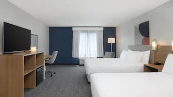 A hotel room with two beds, a desk, a chair, a TV, and a window with curtains.