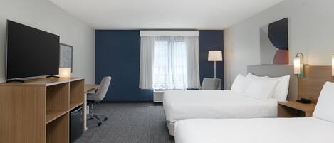 Habitación de hotel con dos camas, un escritorio, una silla, un televisor y una ventana con cortinas.