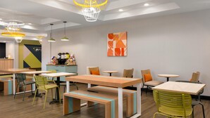 Una cafetería moderna con mesas y sillas de madera, una estación de café y arte abstracto en la pared.